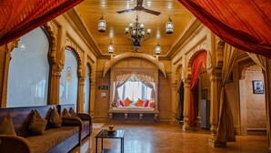 Un hall d’entrée spacieux, doté d’un canapé, d’un lustre et offrant une vue sur l’extérieur à travers une fenêtre ornée de rideaux rouges.