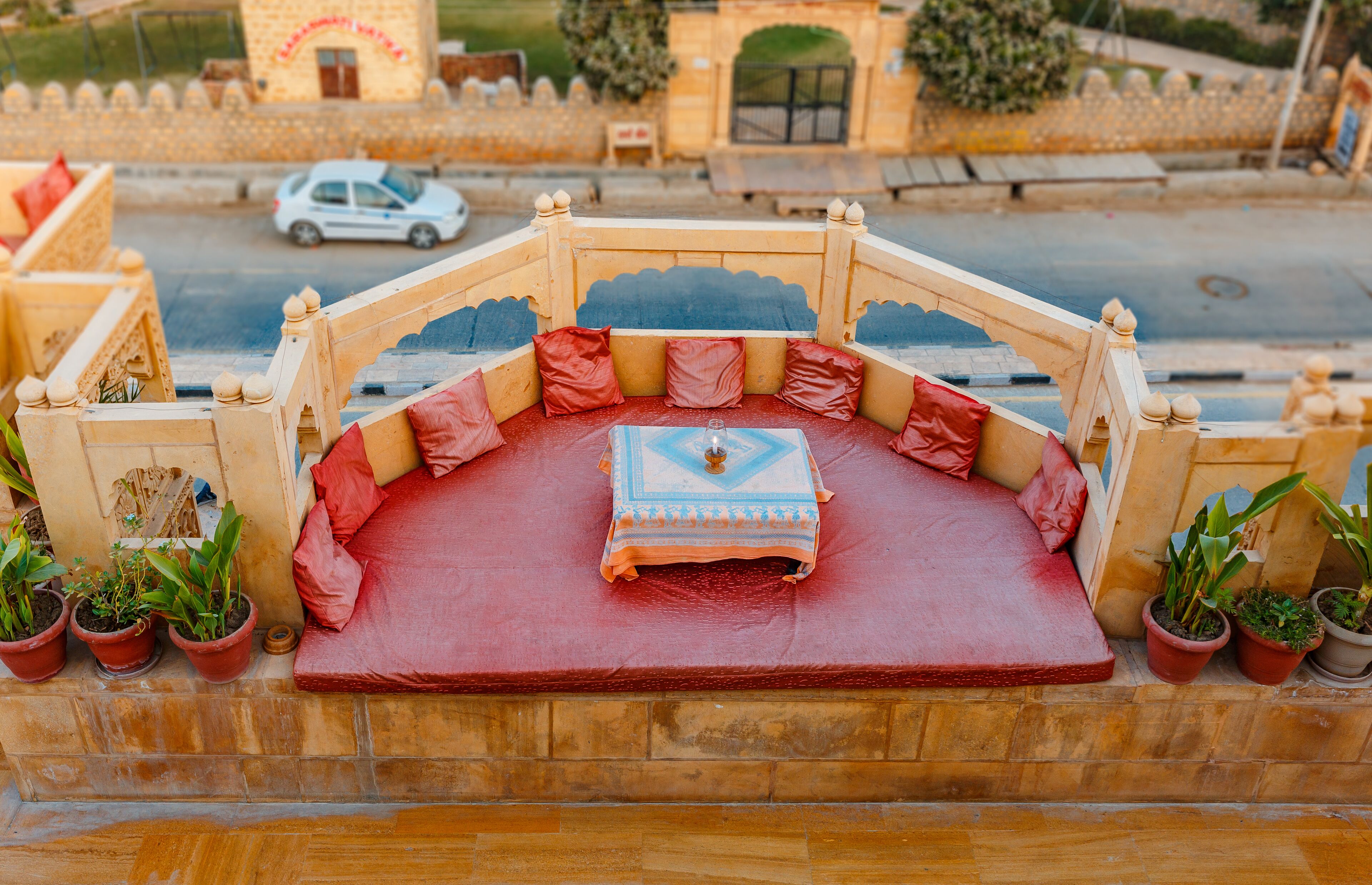 Un espace extérieur aménagé avec des sièges traditionnels, comprenant un coussin rouge, un coussin à motifs bleus et plusieurs plantes en pot.