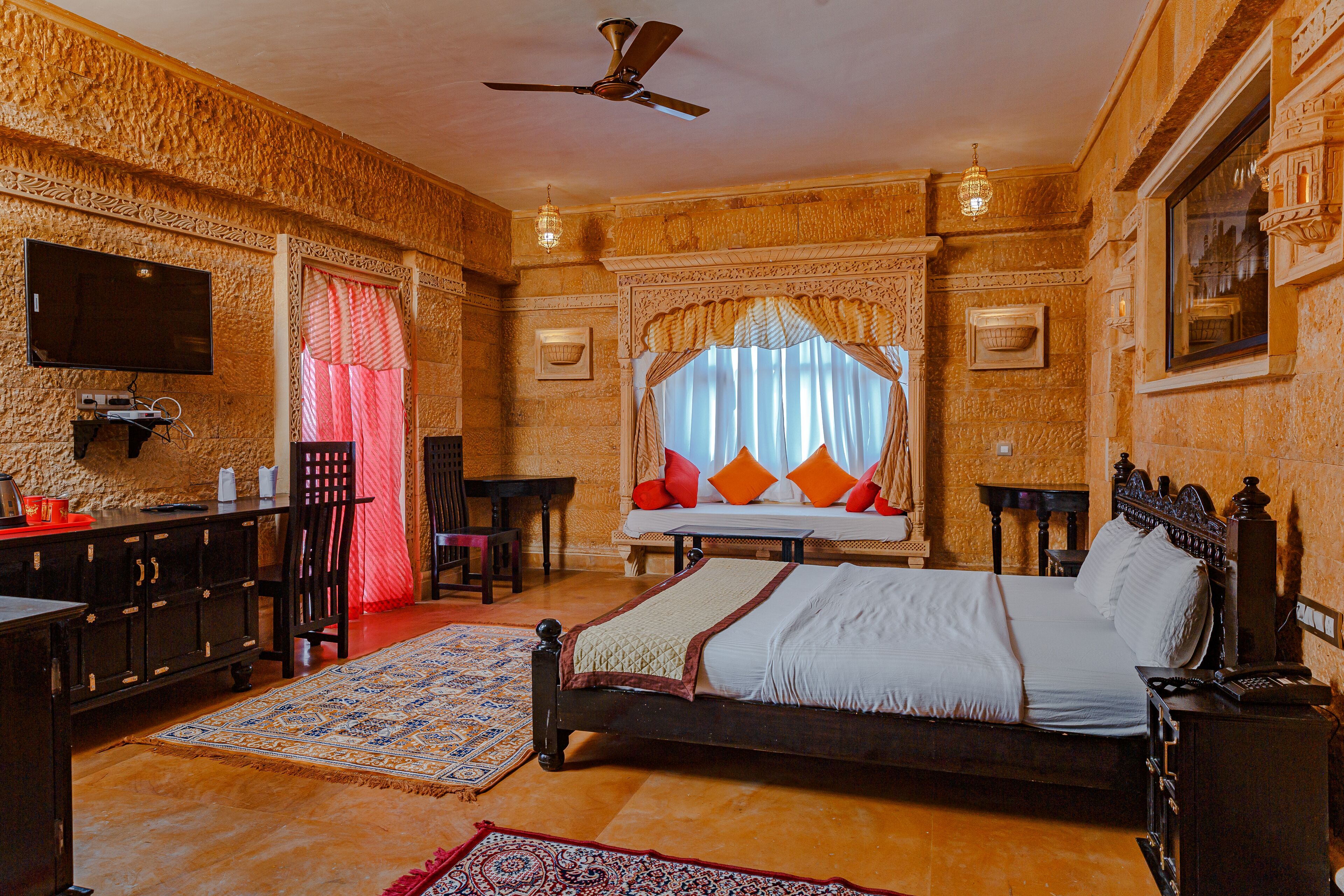 A traditional room with a bed, a desk, a television, and a ceiling fan.
