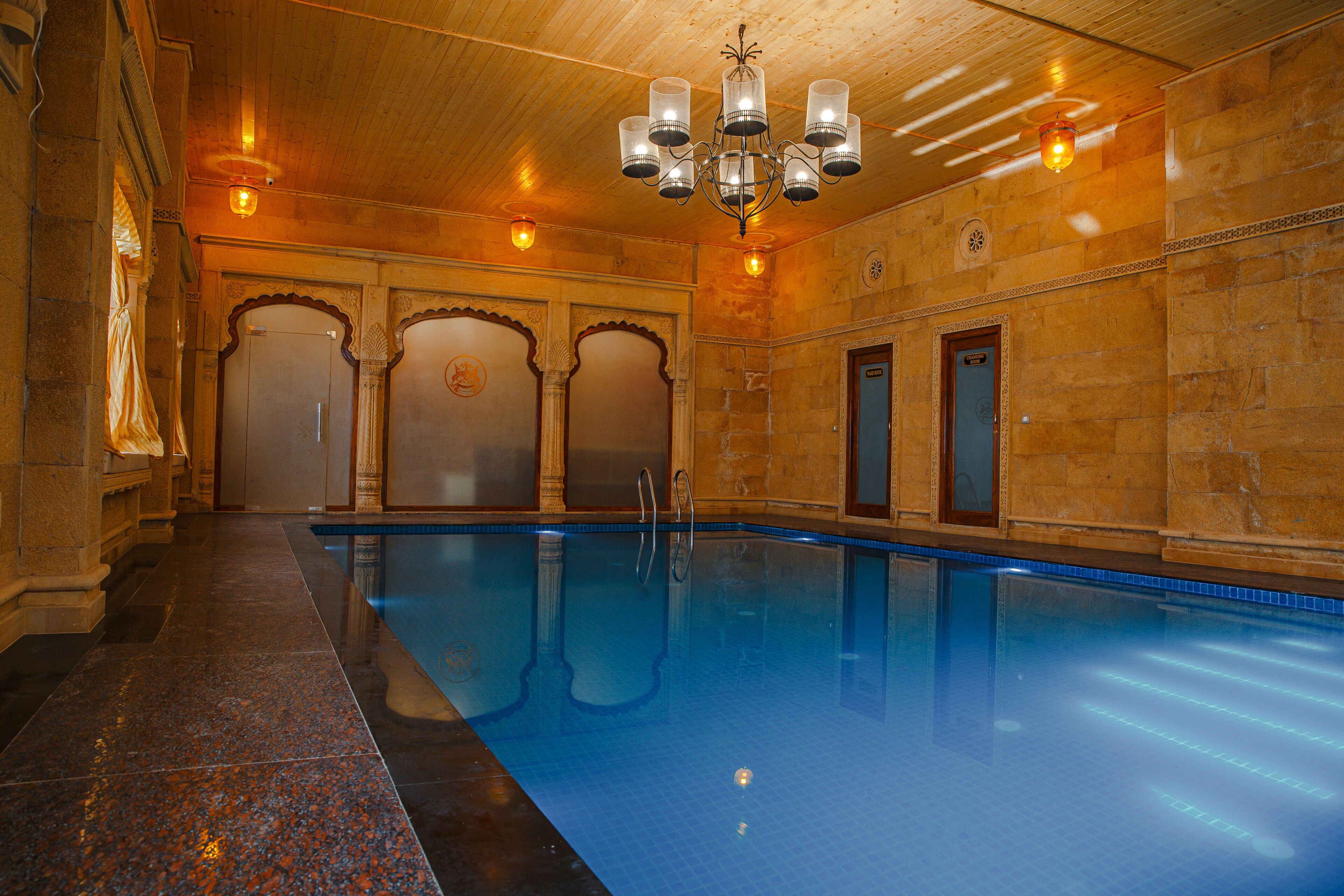 An indoor swimming pool with a wooden ceiling, stone walls, and a chandelier.