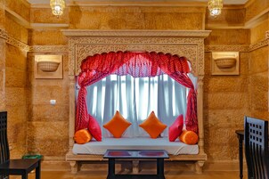 Una habitación con un ventanal decorativo, un sofá con cojines naranjas y una mesa en primer plano.