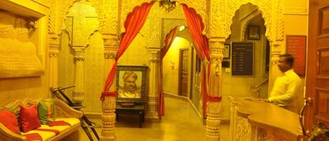 An ornate room with a sofa, a framed portrait, and a reception desk.