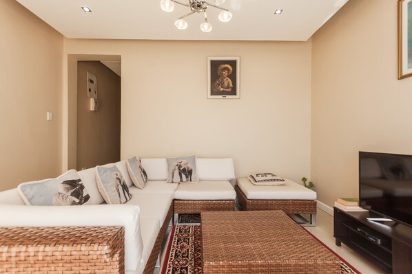 A modern living room with a sofa, ottoman, TV, and artwork on the wall.