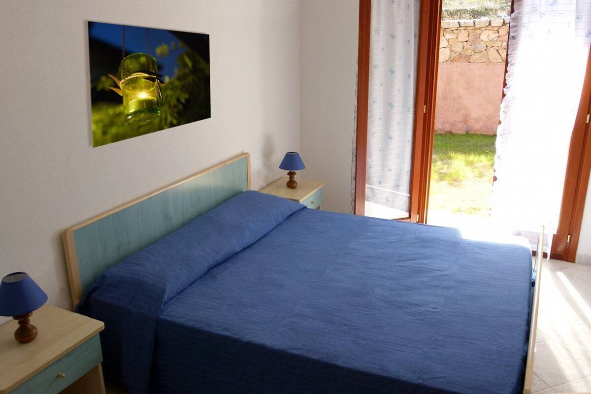 A bedroom with a bed, two bedside tables with lamps, a picture on the wall, and a view of the outdoors.
