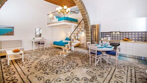 A spacious loft-style apartment with a high ceiling, a mezzanine bedroom, a kitchen with white cabinets, and a patterned carpet. - The Red Door in Koskinou (Rhodes)