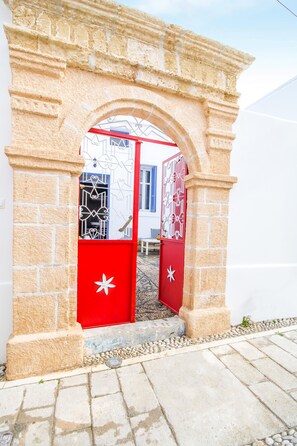 An entrance with a stone archway and red doors with white star designs. - The Red Door in Koskinou (Rhodes)