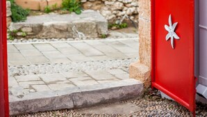 A red door with white decorative patterns, leading to an outdoor area with stone walls and a paved path. - The Red Door in Koskinou (Rhodes)