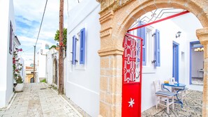 A narrow street with white buildings, a red door, and a small table with chairs. - The Red Door in Koskinou (Rhodes)