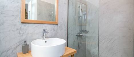 A modern bathroom with a marble sink, wooden vanity, and a glass shower enclosure.
