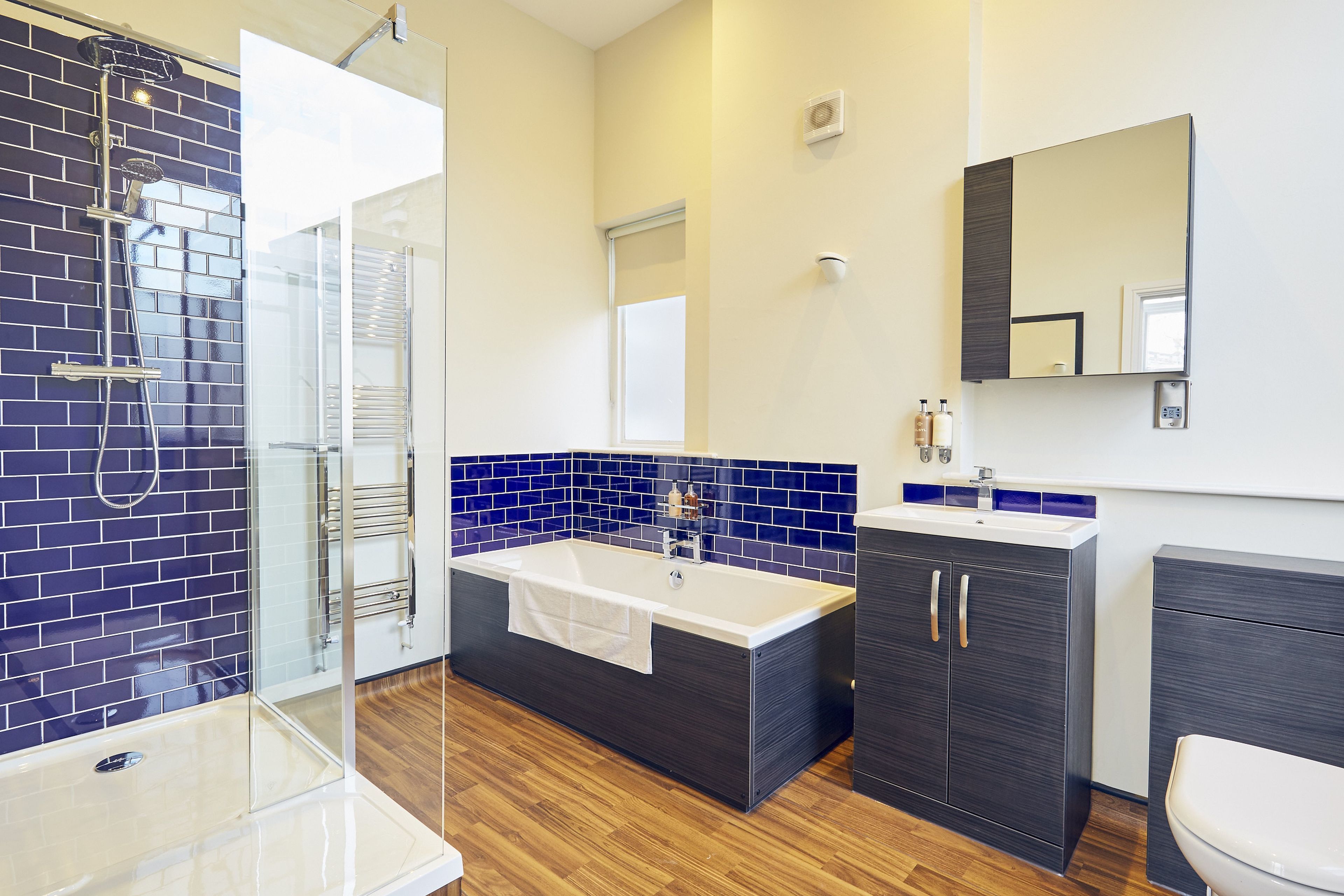 A modern bathroom with a glass-enclosed shower, a freestanding bathtub, a dark wooden vanity, and a white toilet.