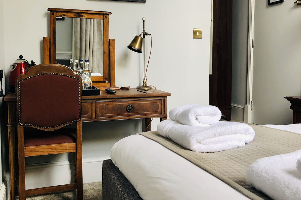 Quarto de hotel com cama, escrivaninha, cadeira, abajur e espelho.