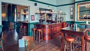 Una zona de bar con taburetes de madera, una barra y un espejo en la pared.