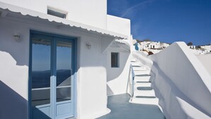 A white building with a blue door and a staircase leading to a higher level. - Aspa Caves (Santorini)