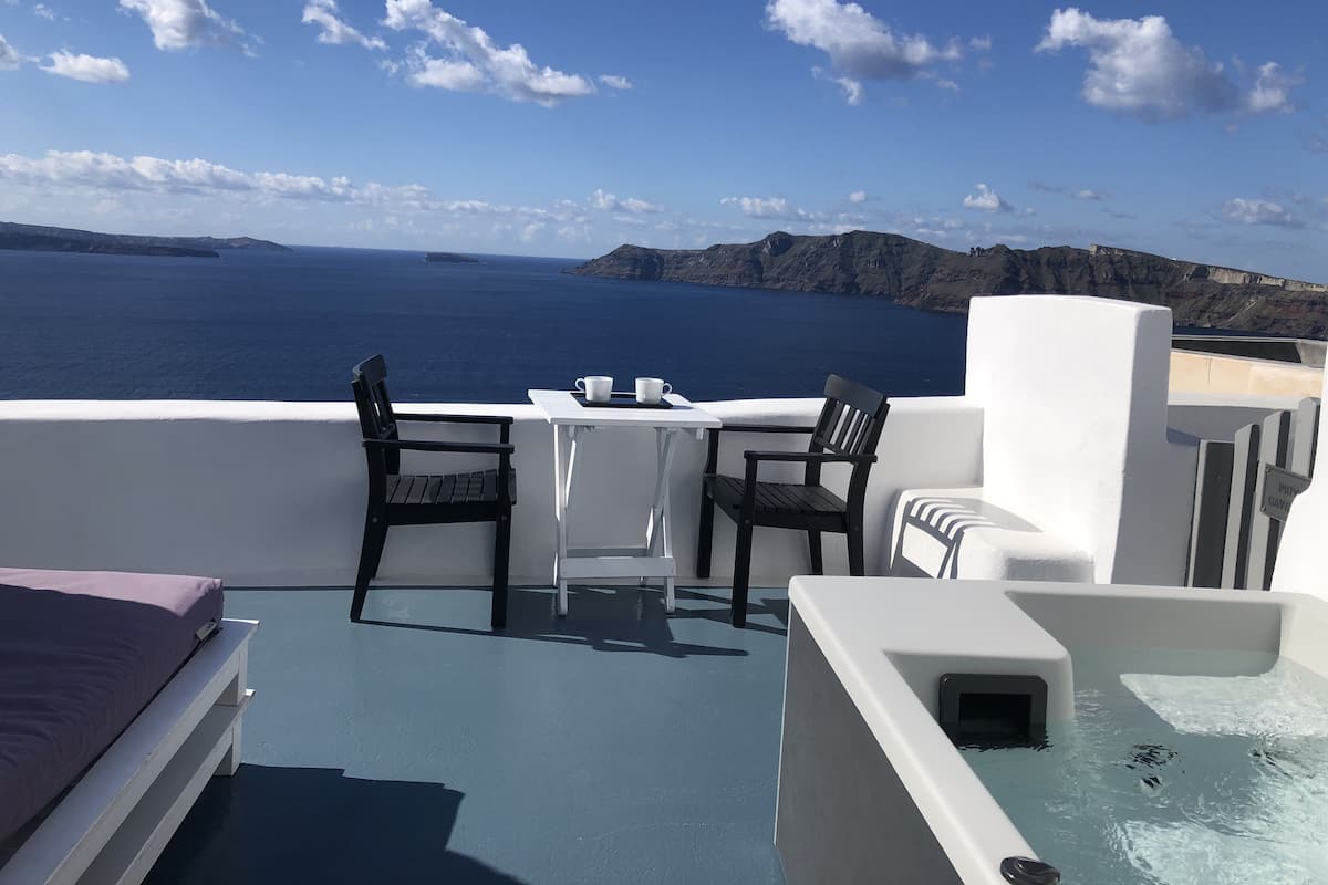 A balcony with a table and chairs overlooking a body of water and distant landforms.