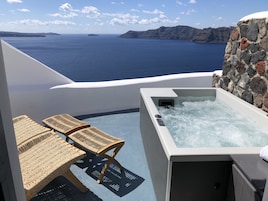 Un jacuzzi con un muro de piedra de fondo, con vista a un cuerpo de agua y terreno distante.
