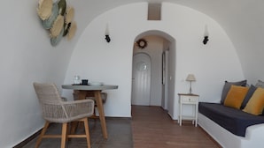 A modern living room with a sofa, a dining table with chairs, and a small side table. - Aspa Caves (Santorini)