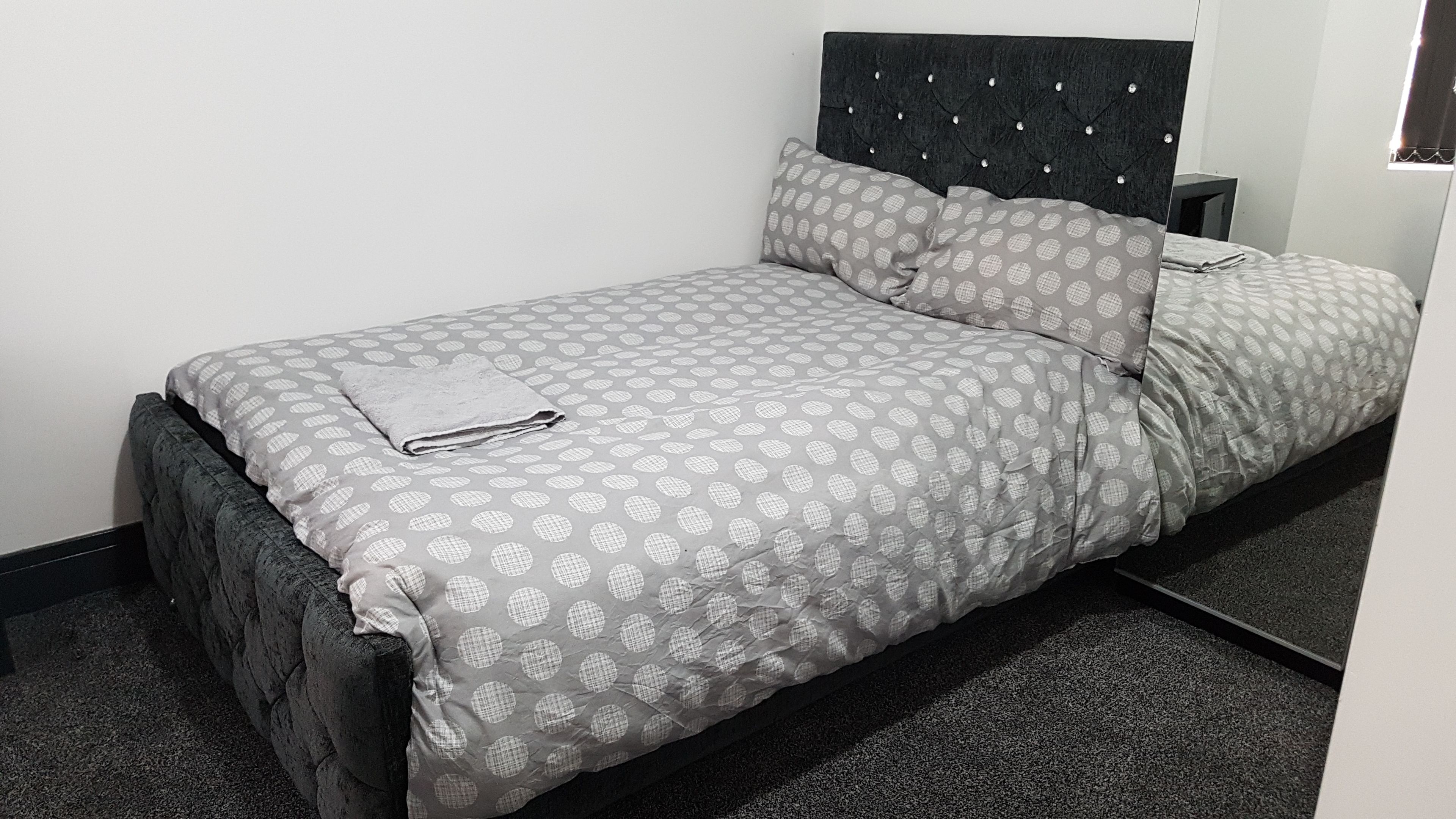 A single bed with a patterned bedspread and pillows, a dark headboard, and a small bedside table.
