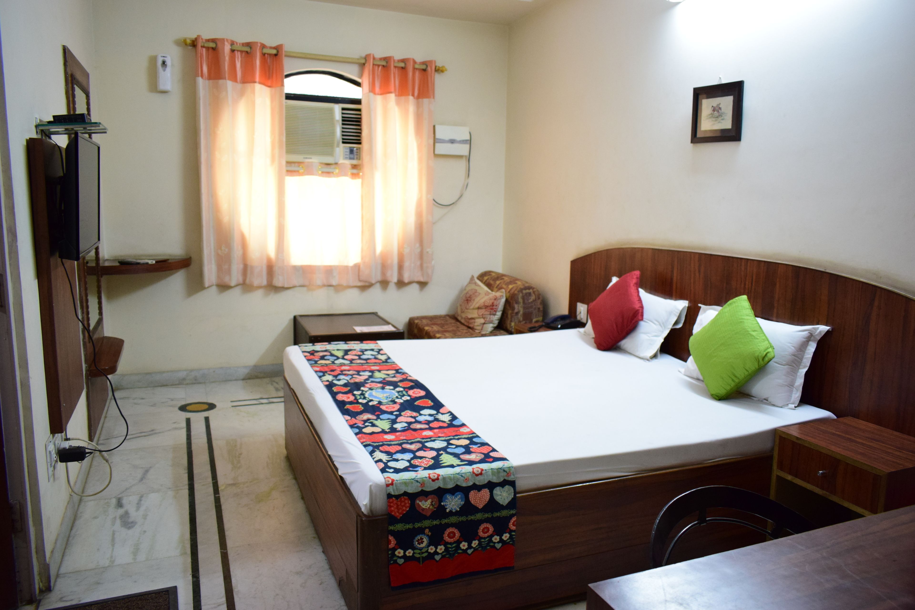 A bedroom with a bed, bedside tables, a TV, and a window with curtains.