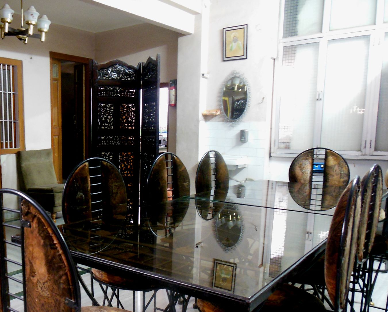 A dining area with a glass table and metal chairs, a decorative black partition, and a white wall with a framed picture.