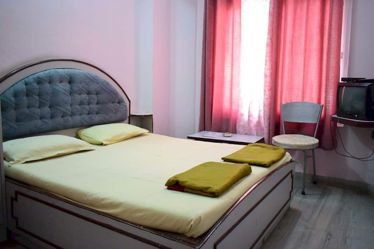 Una cama individual con cabecera, una mesita de noche, una silla y un televisor.