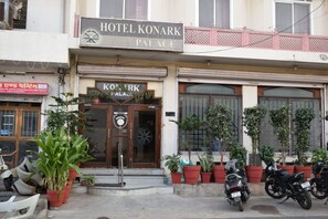 Un hotel llamado HOTEL KONARK PALACE con un letrero, plantas en macetas y motocicletas estacionadas al frente.