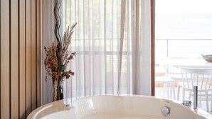 A bathroom with a bathtub, a white sink, and a window with sheer curtains. - Elia Seaside Nea Chora (Chania)