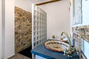A bathroom with a stone wall, a glass shower enclosure, and a sink with a decorative basin. - Dreams Alpujarra (Carataunas)