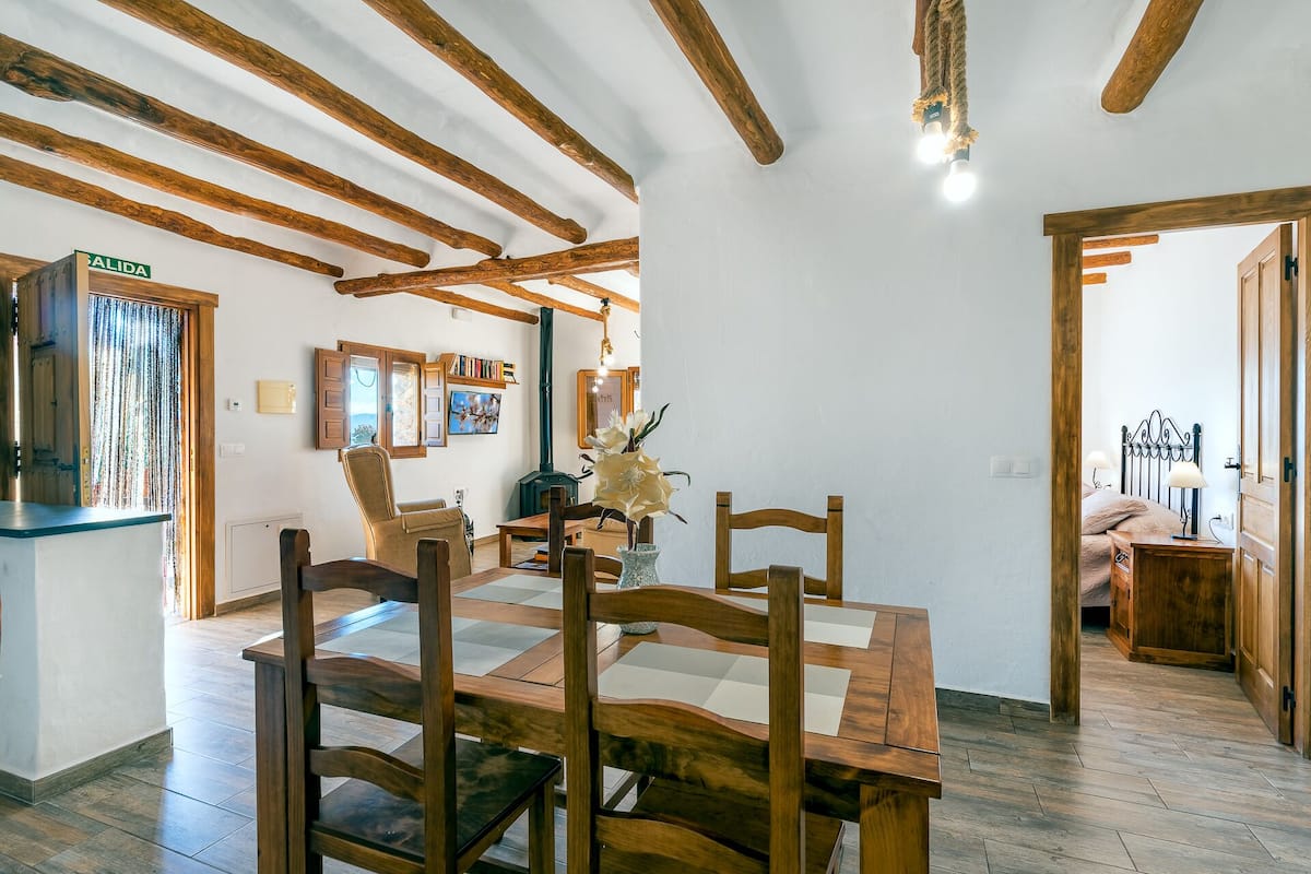 Un coin repas avec une table et des chaises en bois, une cheminée et une vue sur la cuisine.
