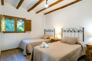 A bedroom with two beds, wooden beams on the ceiling, a window with shutters, and a bedside table with a lamp. - Dreams Alpujarra (Carataunas)