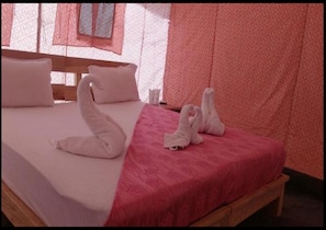 A bed with a pink bedspread and white pillows. There are two white towels folded on the bed.