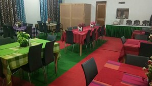 A conference room with multiple tables and chairs, green and red tablecloths, and a green carpet. - Pangong Heritage Camp (Leh)