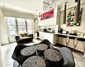 A modern kitchen with white cabinets, a microwave, and a coffee machine. There is a dining area with black chairs and patterned table mats. - Soho Suite London (London)