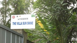 Un letrero que dice 'The Villa Sun Shine' con una bandera alemana, una cruz médica y un símbolo medioambiental.