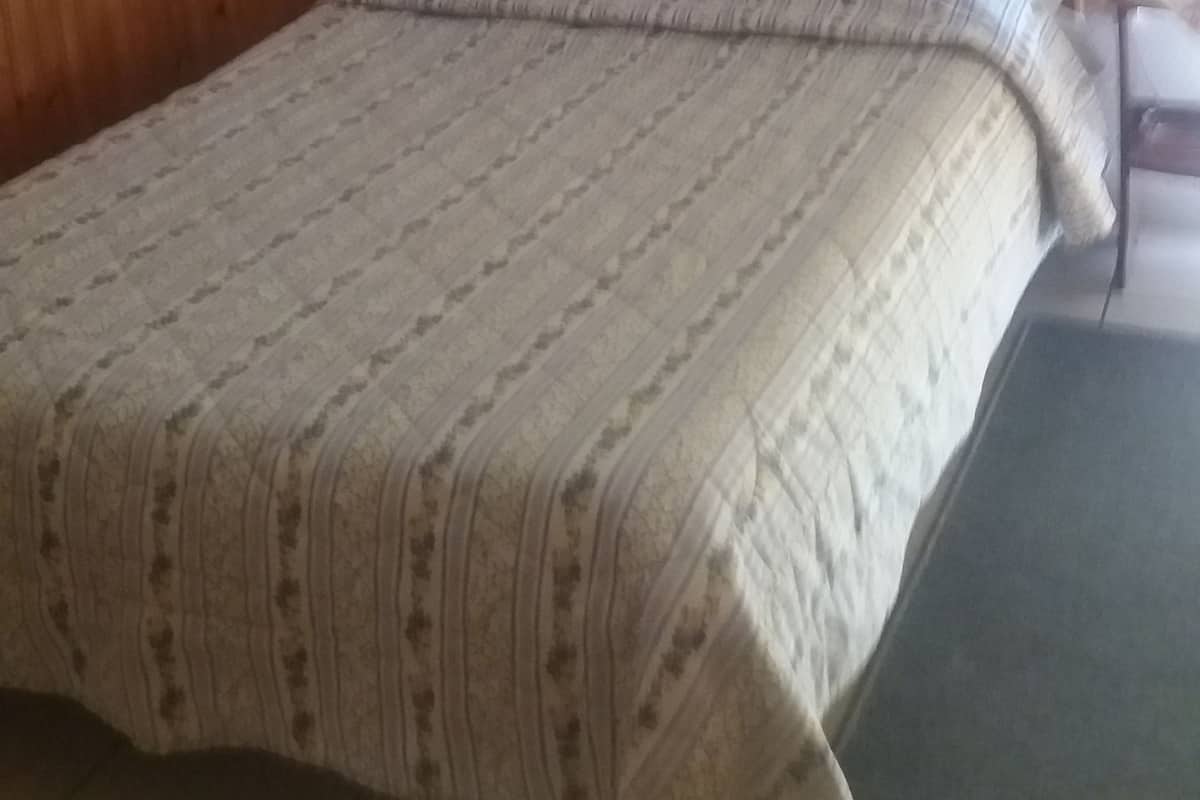 Un dormitorio con cabecera de madera, cama con colcha estampada, mesita de noche y unidad de aire acondicionado montada en la pared.