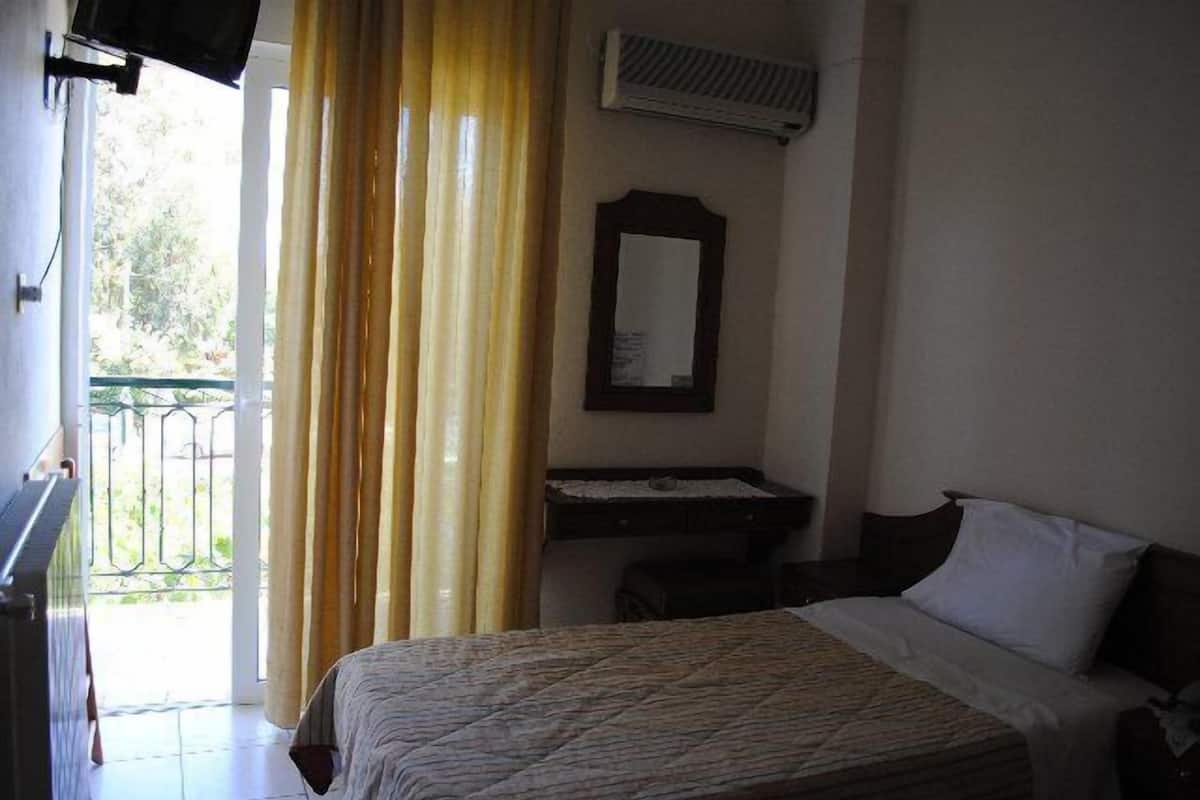 Un dormitorio con cama, escritorio, silla, espejo y ventana con cortinas.