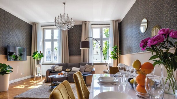 En moderne stue med en sofa, spisebord dækket til to personer og en lysekrone.