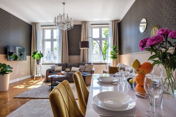 En moderne stue med en sofa, spisebord dækket til to personer og en lysekrone.