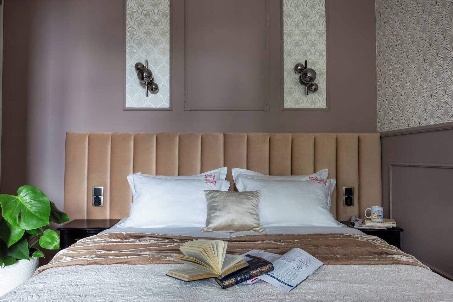 Habitación de hotel con una cama grande, una mesita de noche, una planta y un aplique de pared.