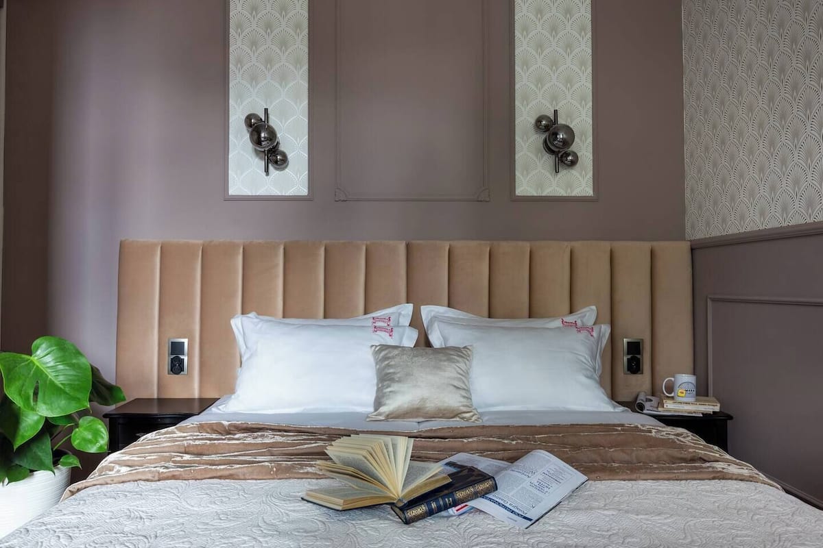 Habitación de hotel con una cama grande, una mesita de noche, una planta y un aplique de pared.