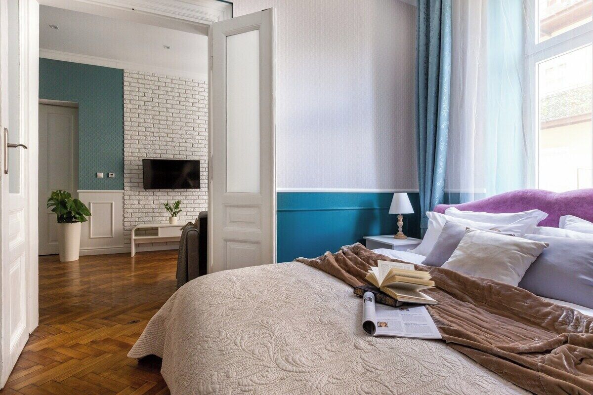A hotel room with a bed, a TV, a desk with a computer, and a window with curtains.