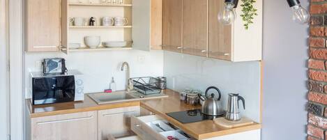 Cocina compacta con armarios de madera, un tostador integrado, un lavabo y una tetera.