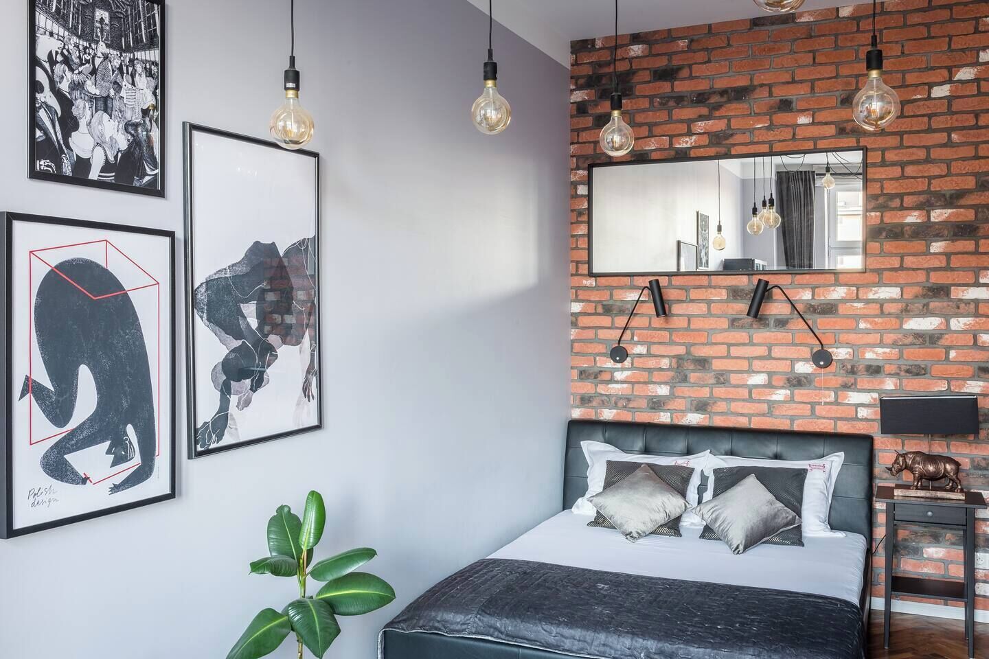 Ein Schlafzimmer mit Backsteinwand, einem Bett mit Kissen, einer Pflanze und gerahmten Kunstwerken.