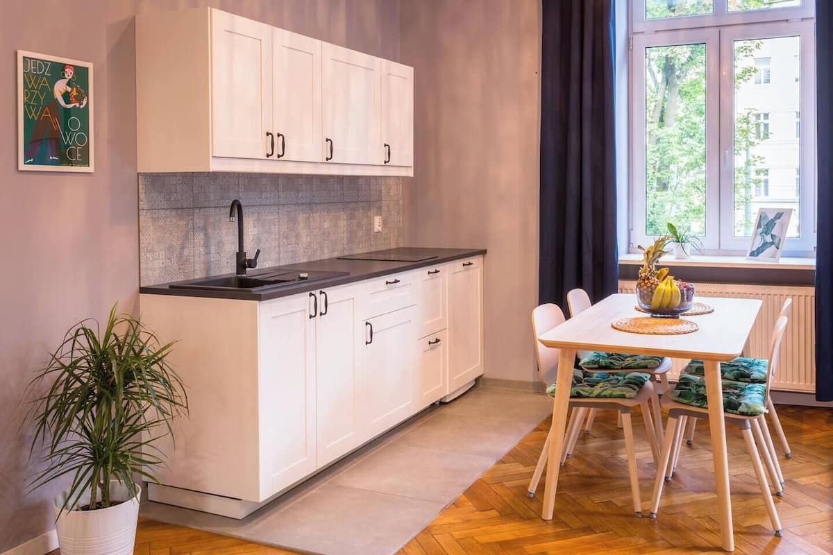 Una cocina moderna con armarios blancos, encimera negra y una zona de comedor con mesa y sillas.
