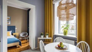 Et værelse med en seng, et spisebord med stole, et vindue med gardiner og en hængende lampe.