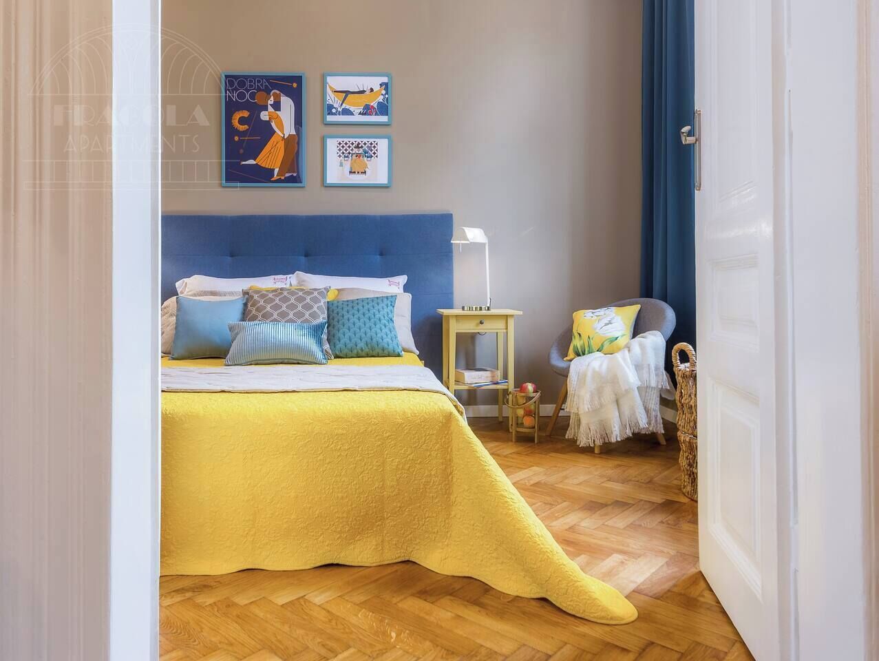 A bedroom with a bed, bedside table, chair, and artwork on the wall.