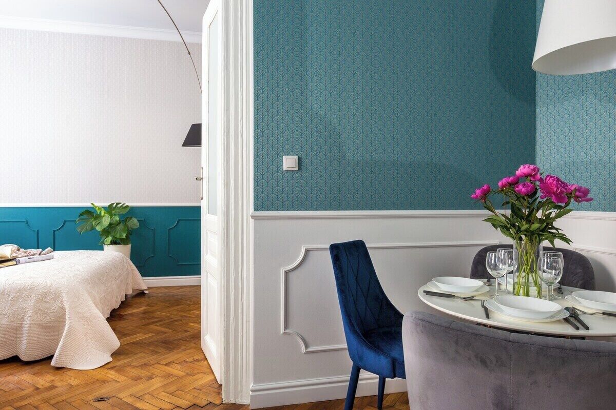 A dining area with a table set for four, a blue chair, and a vase with flowers.