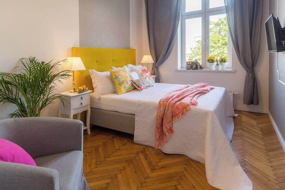 Une chambre à coucher avec un lit, des tables de chevet, une lampe, une plante en pot et une fenêtre avec des rideaux.