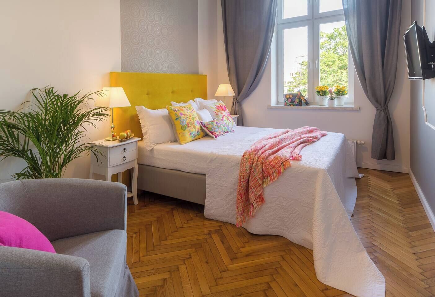 Un dormitorio con cama, mesitas de noche, una lámpara, una planta en maceta y una ventana con cortinas.