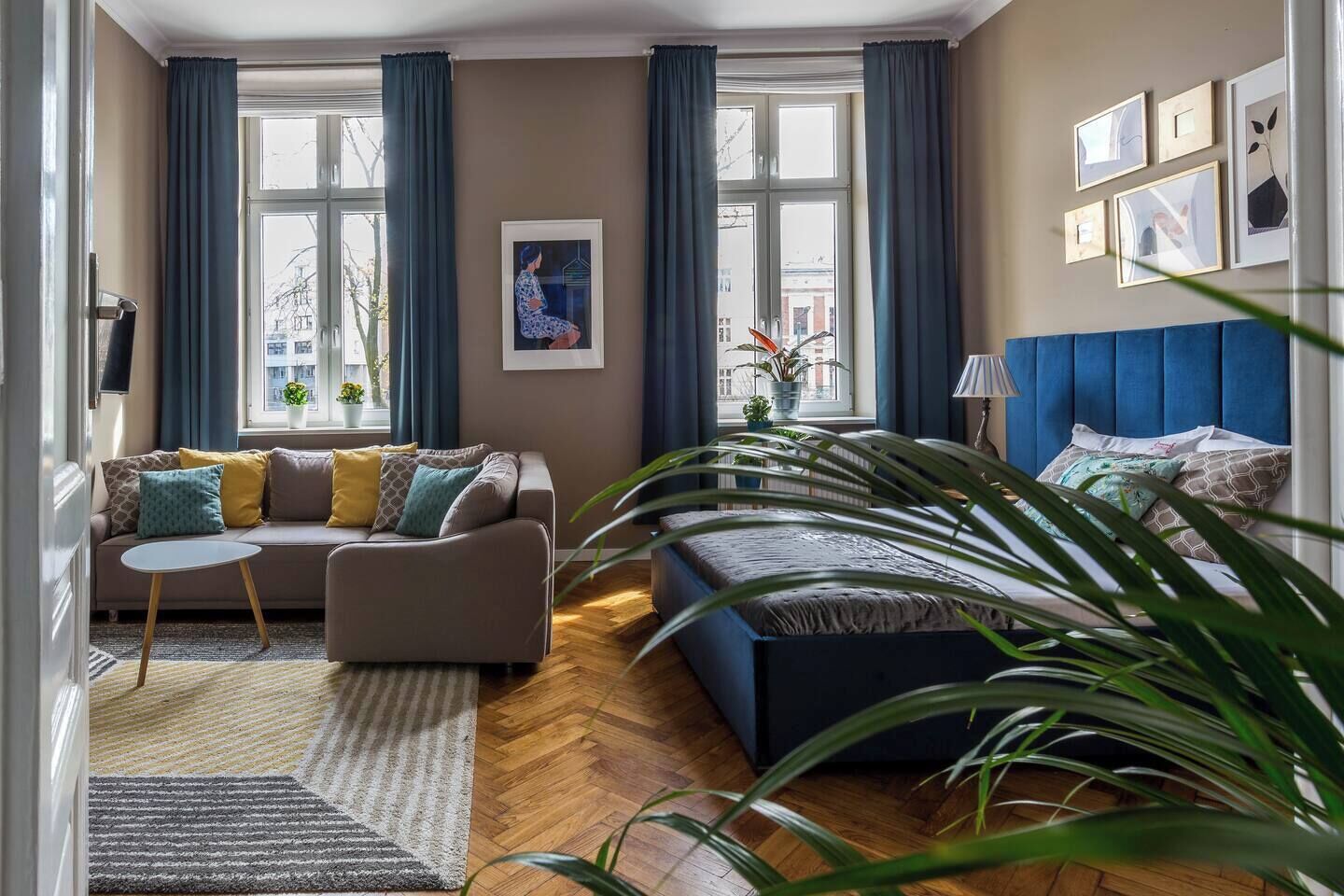 Ein Wohnzimmer mit einer Couch, einem kleinen Tisch, einem blauen Sofa und einer großen Pflanze.