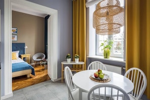 Une pièce comprenant un lit, une table à manger avec des chaises, une fenêtre avec des rideaux et un luminaire suspendu.
